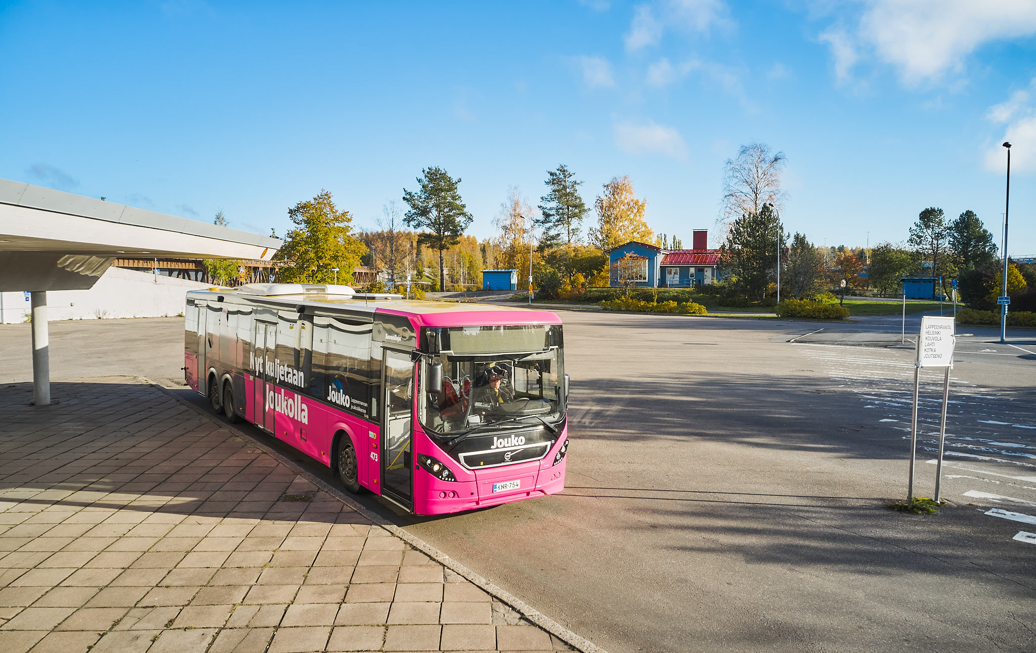 Pinkki Jouko-bussi parkissa syksyisessä maisemassa.